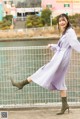 A woman in a purple dress and green boots leaning against a fence.